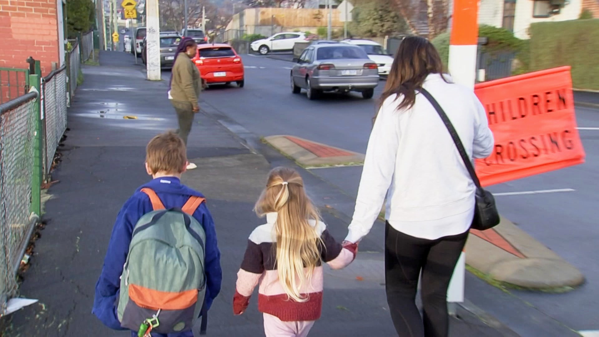 A mother holds her daughter's hand as she walks two kids to school.
