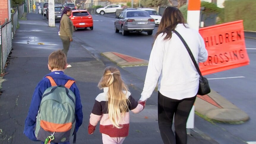 A mother holds her daughter's hand as she walks two kids to school.