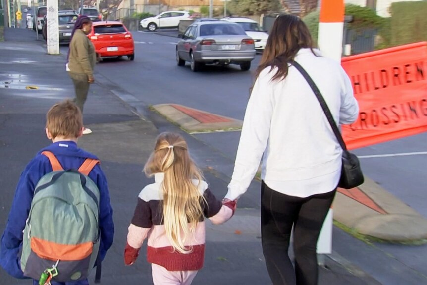 A mother holds her daughter's hand as she walks two kids to school.