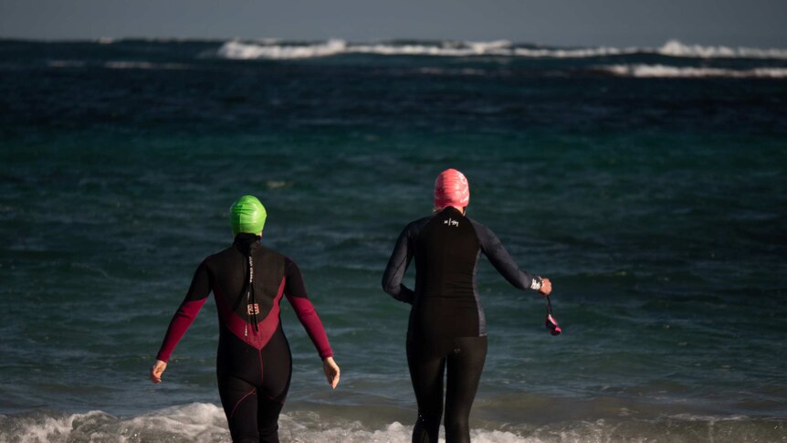 two women in wetsuits walk into the ocean