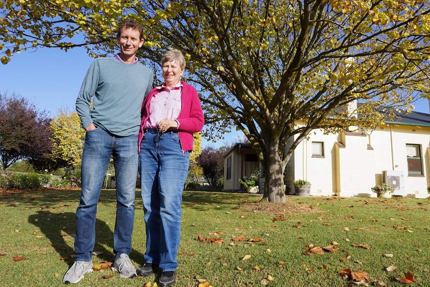 Michael Waite, a tall slender man, stands smiling next to his mother Sue by a large oak tree in her Naracoorte backyard.