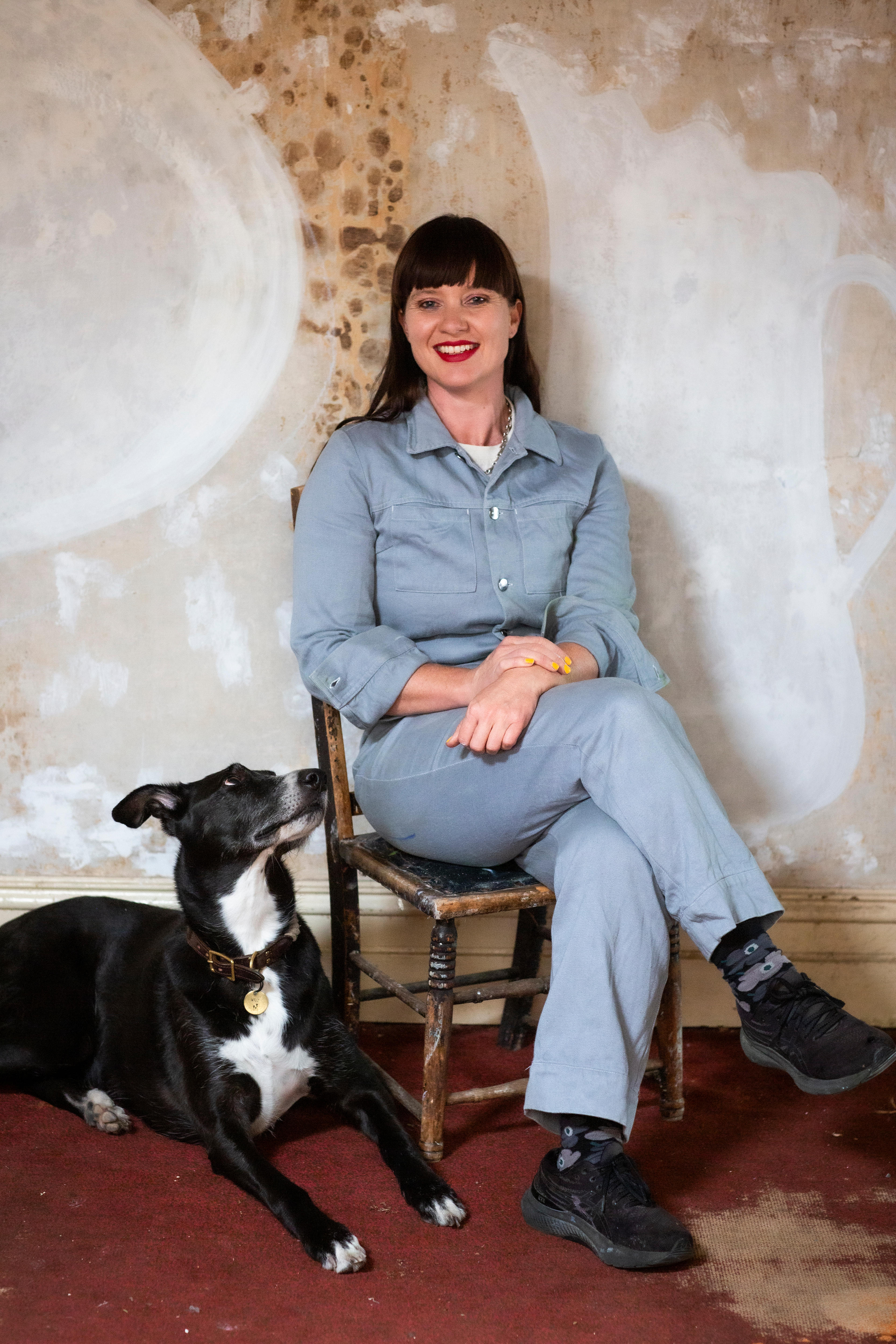 A woman and her dog sit in front of a weathered, painted wall