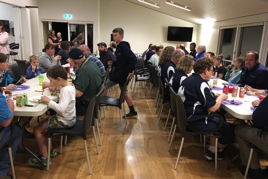 Dozens of people sitting down at two long tables having dinner