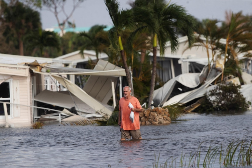 A person wearing an orange t-shirt wades into flood water in a hurricane-ravaged street.