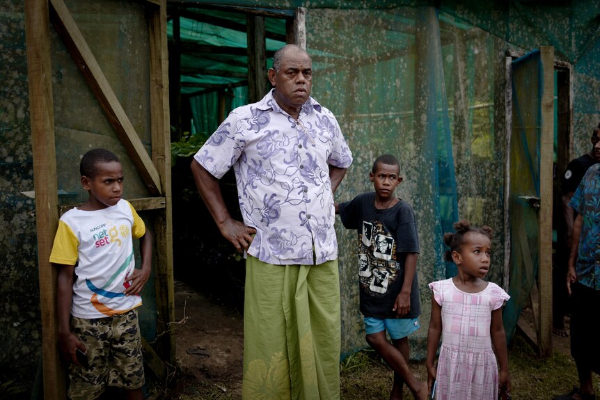 A man stands in front of a green house, near three children. 