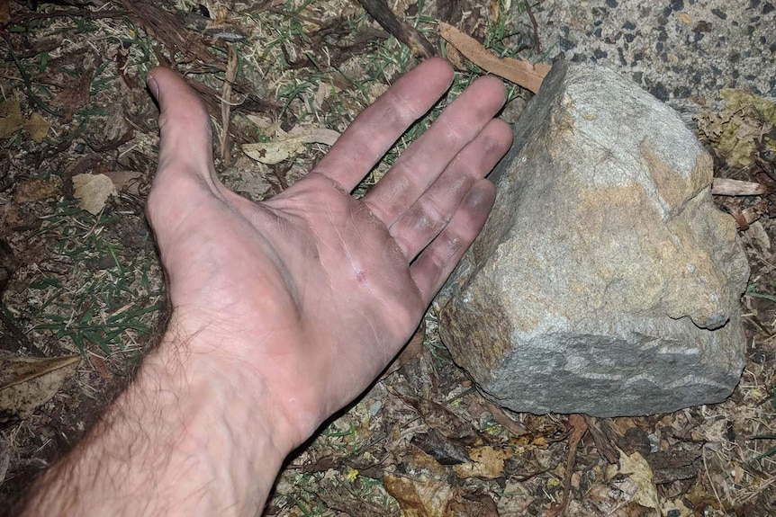 A hand lying on the ground next to a large rock