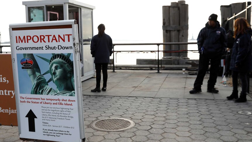 people stand behind a sign indicating the statue of liberty and ellis island has closed due to a government shutdown