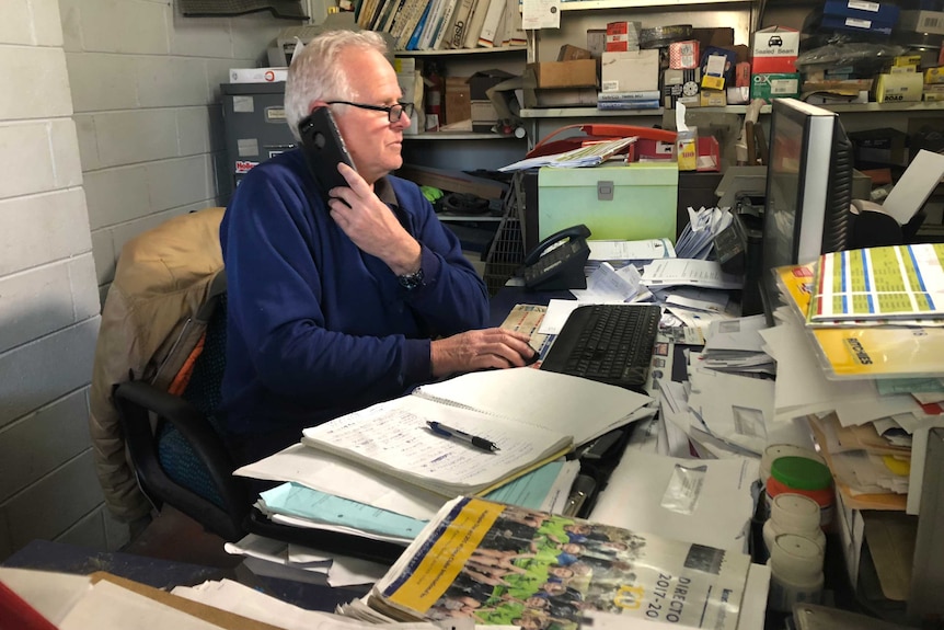 Graham Cockerell speaks on his mobile while sitting at a computer in his office.