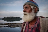 Portrait of 75-year-old man looking out to sea at dusk.