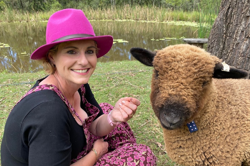 A lady in a pink had smiling at the camera with a sheep smiling at the camera next to her. 