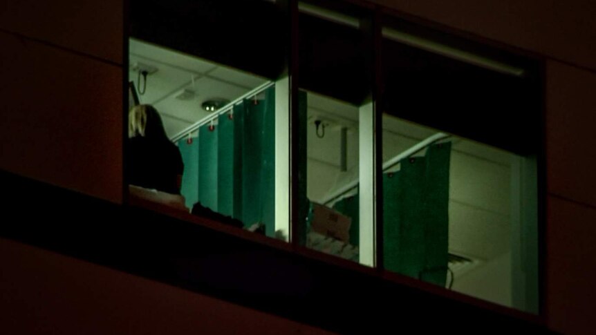 Back of woman's head visible through hospital room window with curtain visible