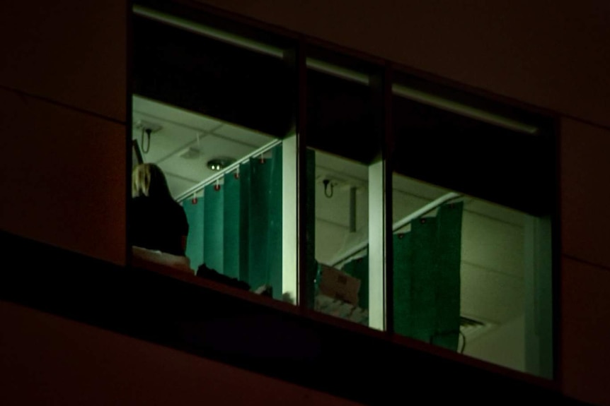 Back of woman's head visible through hospital room window with curtain visible