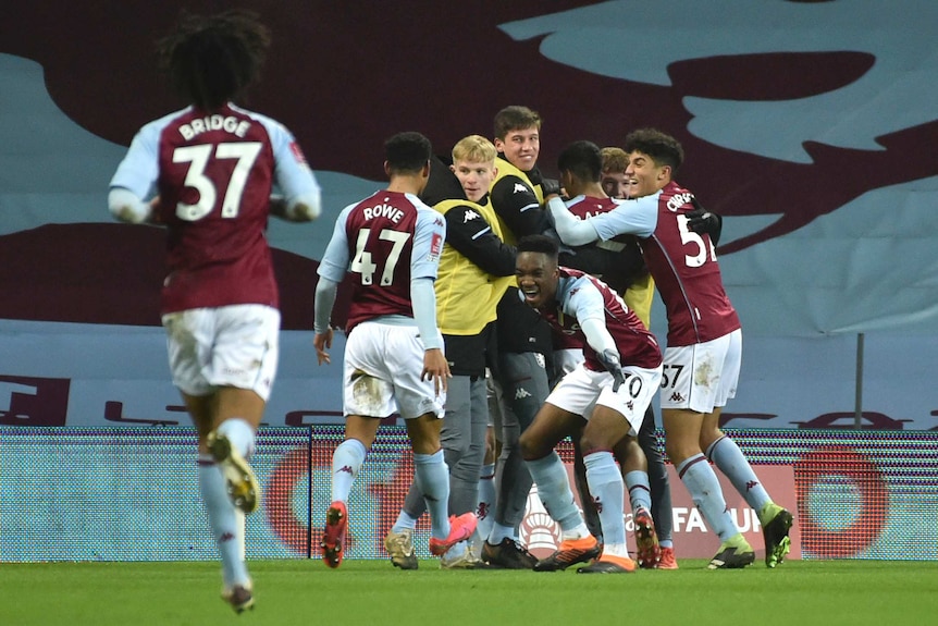 Players wearing claret and blue jerseys celebrate on a pitch.