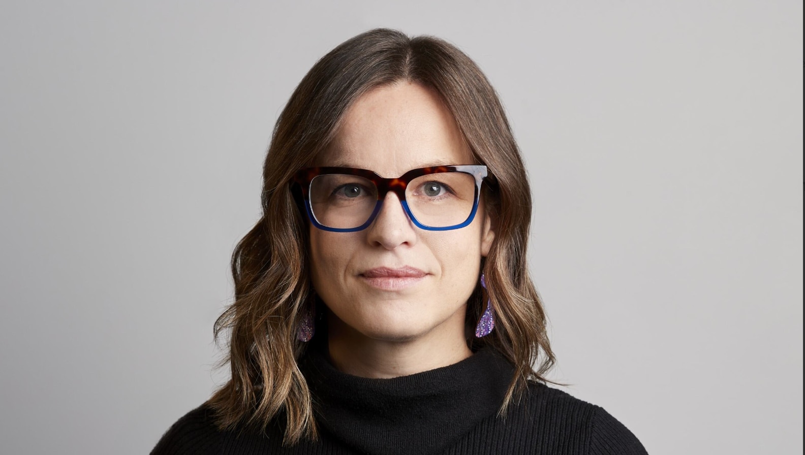 A woman with brown curly hair wearing reading glasses