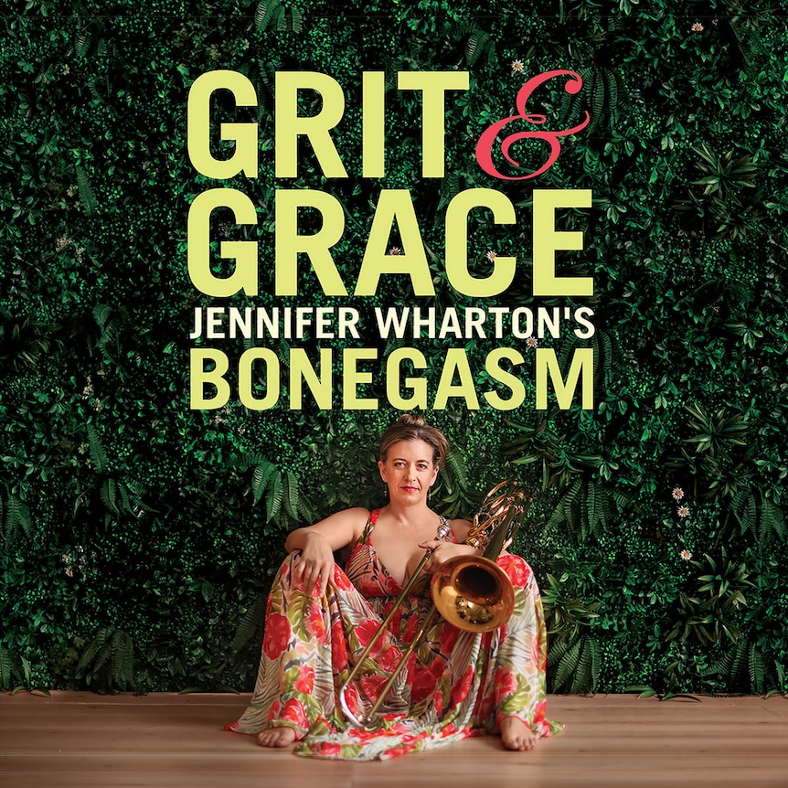 Jennifer Wharton sits in-front of a green, leafy wall in a red dress; she's holding her bass trombone