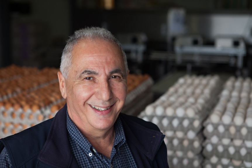 a man is smiling at the camera with cartons of eggs laying behind him 