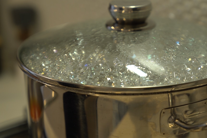 A silver pot with a clear lid is seen with boiling water inside.  