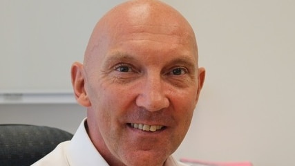A bald man wearing a blue jacket and open-necked shirt