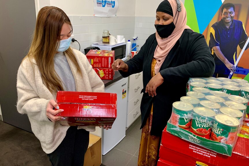 A woman handing another woman a box of food supplies.