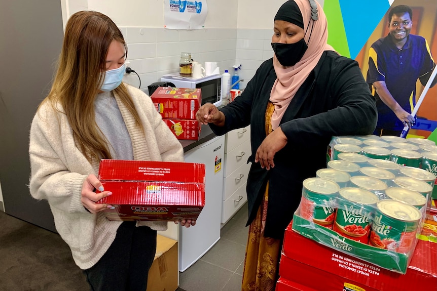 A woman handing another woman a box of food supplies.