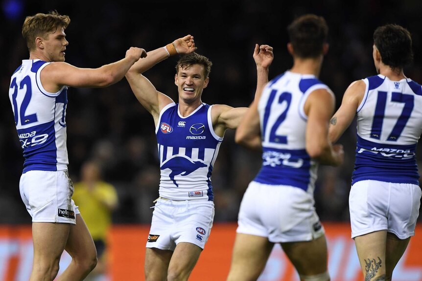 Some AFL players stand next to each other as the goalscorer raises his arms in the air in triumph.