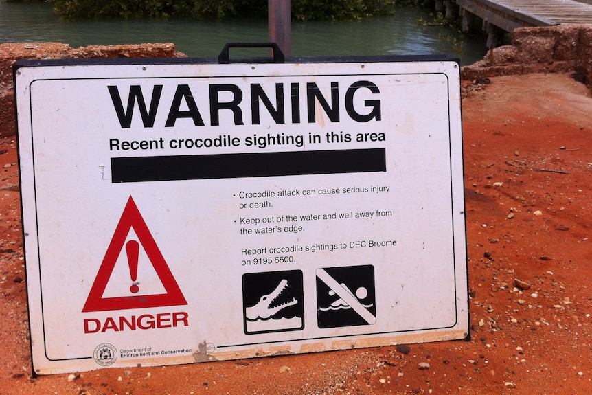 A crocodile warning sign sits on red dirt following a recent crocodile sighting in the area