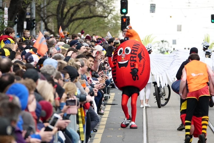 A man dressed in a red Sherrin football suit waves to hundreds of fans lining the street during the grand final parade.