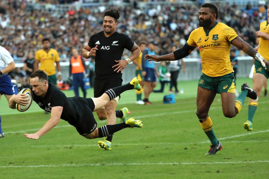 All Blacks' Ben Smith clutched the ball in his right arm as he dives into a try, as an Australian player chases him.