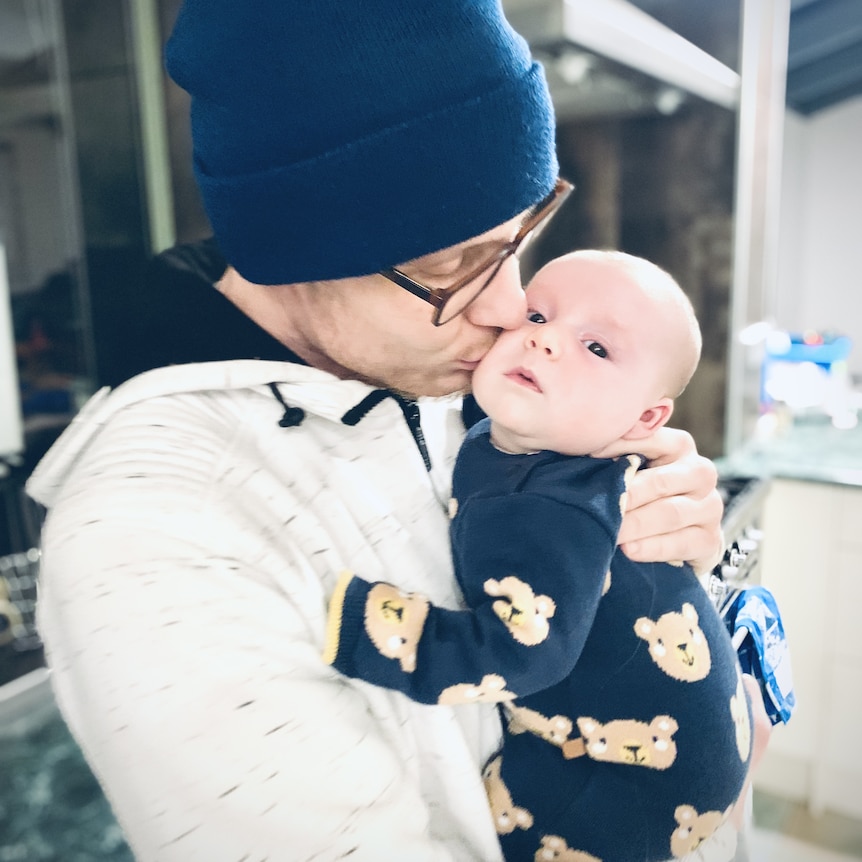 Michael wears a beanie and kisses his baby Lyle.