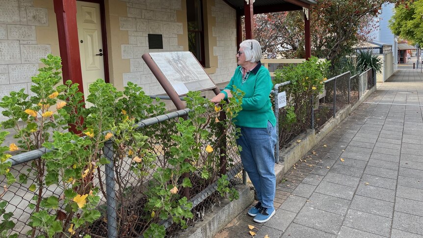 A woman looks at a plaque and an old house