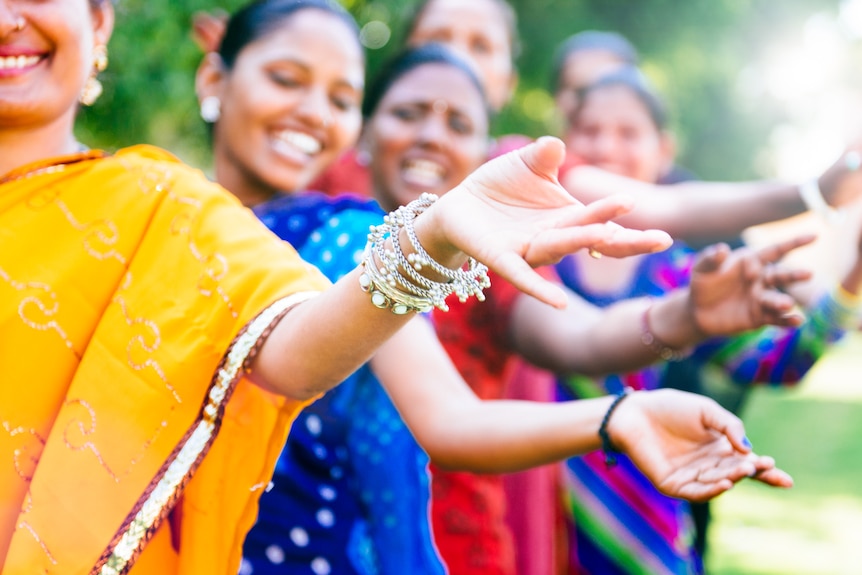 A group of women wearing colourful clothing smile and dance.