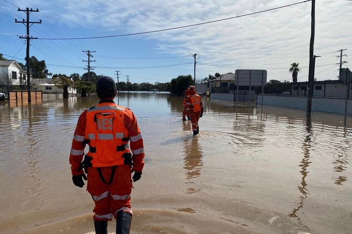 Two men in high-vis walking through floodwaters in a street.