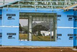A house frame wrapped in blue plastic around large openings where windows should be.