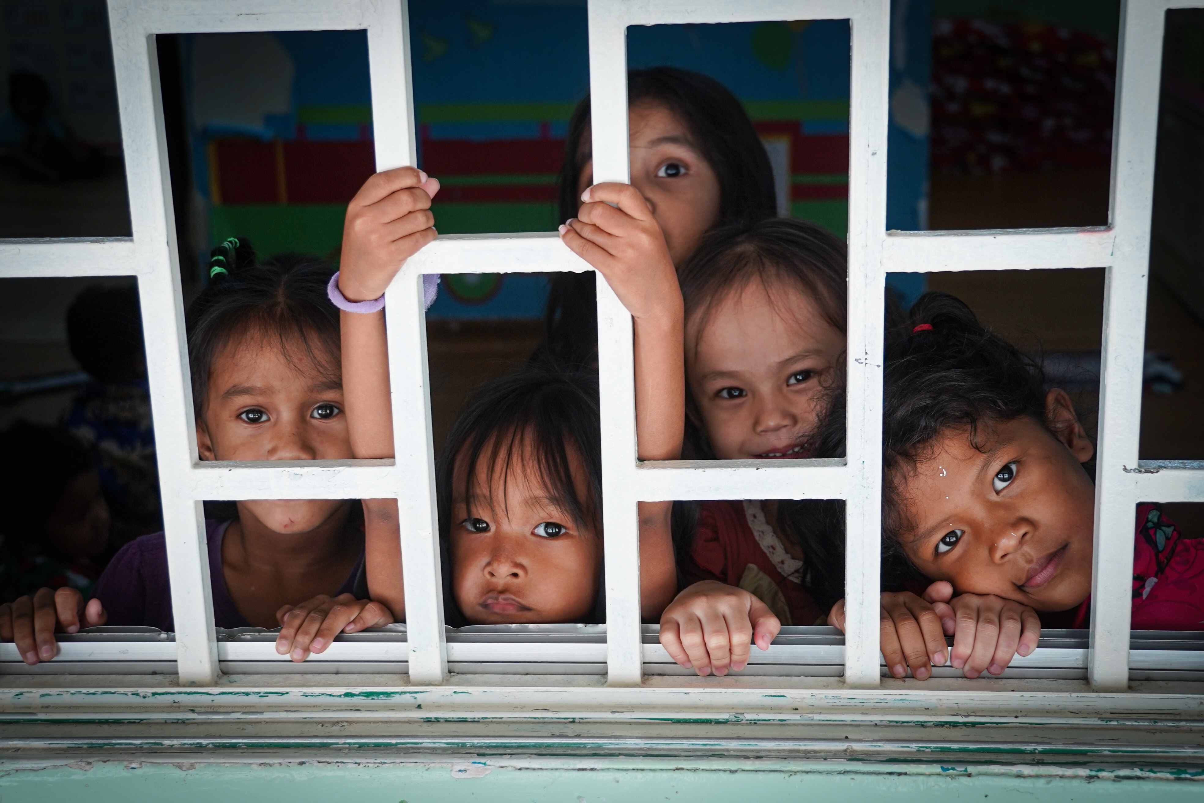 A group of little girls smile through a barred window 