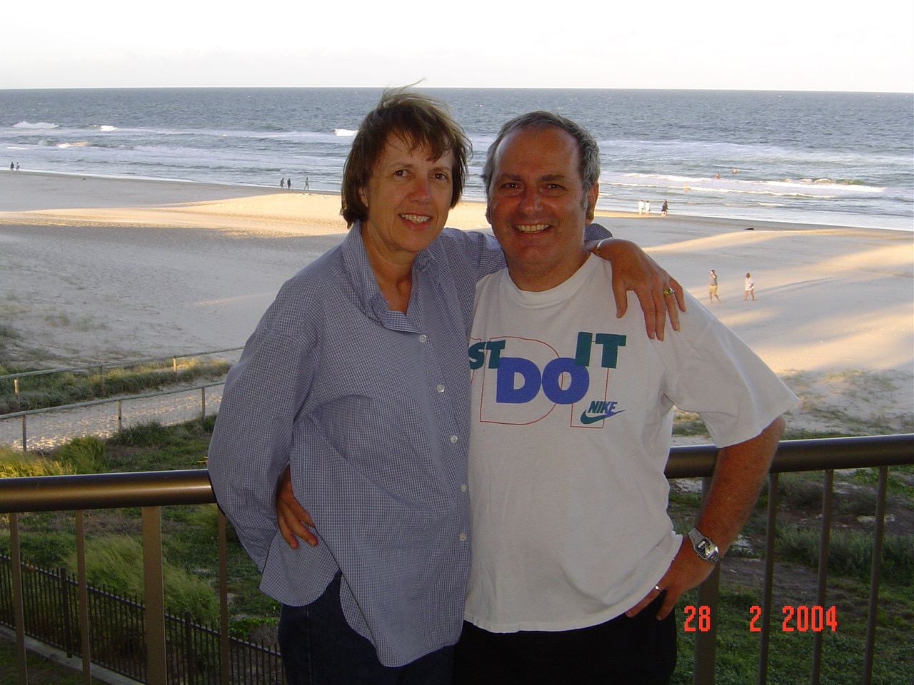A smiling couple on a balcony which overlooks the beach.