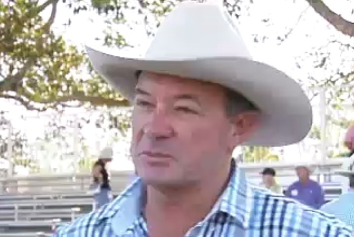 Stud breeder David Bondfield in front of the camera with a white cowboy hat and check shirt in front of some stands at a sale.