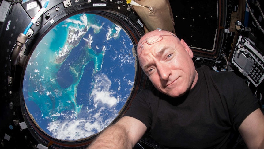 A NASA astronaut takes a selfie with a window, through which the world is seen, in the background