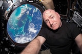 A NASA astronaut takes a selfie with a window, through which the world is seen, in the background