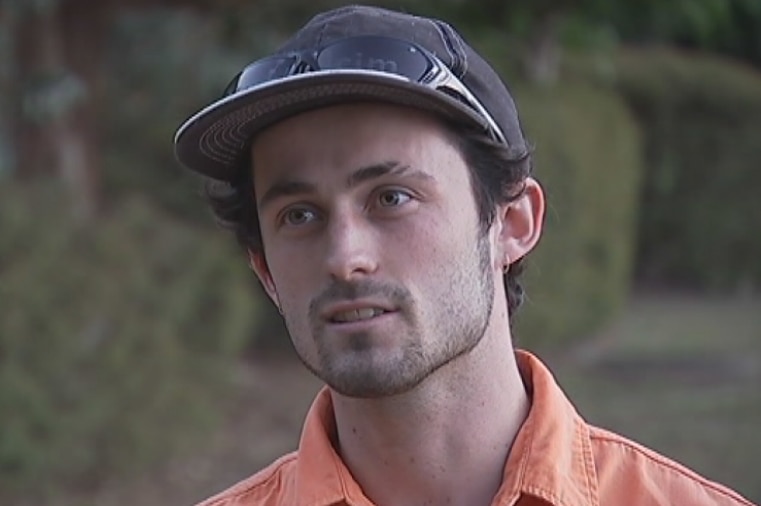 Joseph Brown, a subcontractor, talks to camera. He is wearing an orange shirt, dark cap and sunglasses