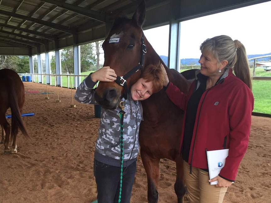 Liam Long hugs a horse used to treat his disability by psychiatrist Anja Kriegeskotten at Samford Riding for the Disabled