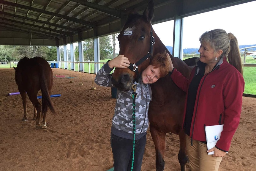 Liam Long hugs a horse used to treat his disability by psychiatrist Anja Kriegeskotten at Samford Riding for the Disabled