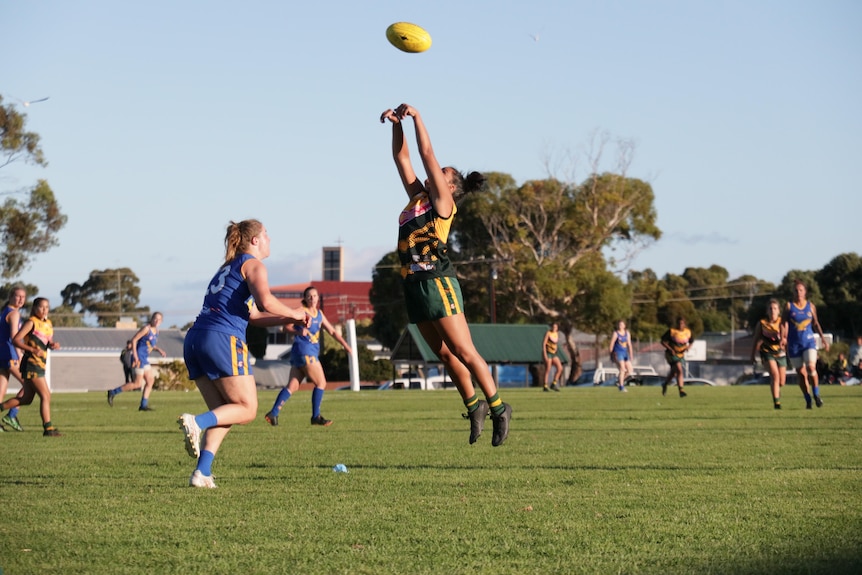 A female footy player jumping high in the air for a ball.