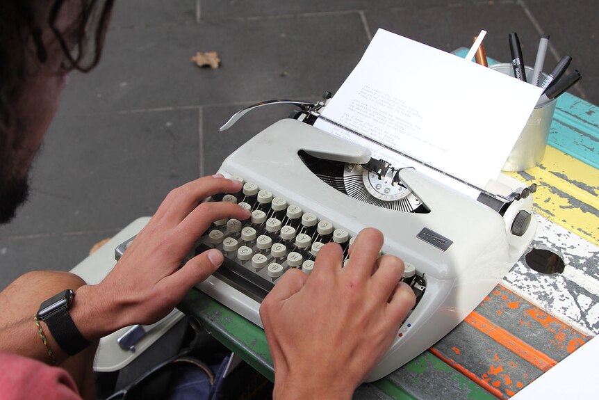 A close up of a man using a grey typewriter.