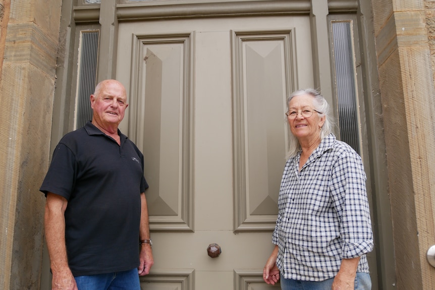 A man and woman stand on either side of a large door.