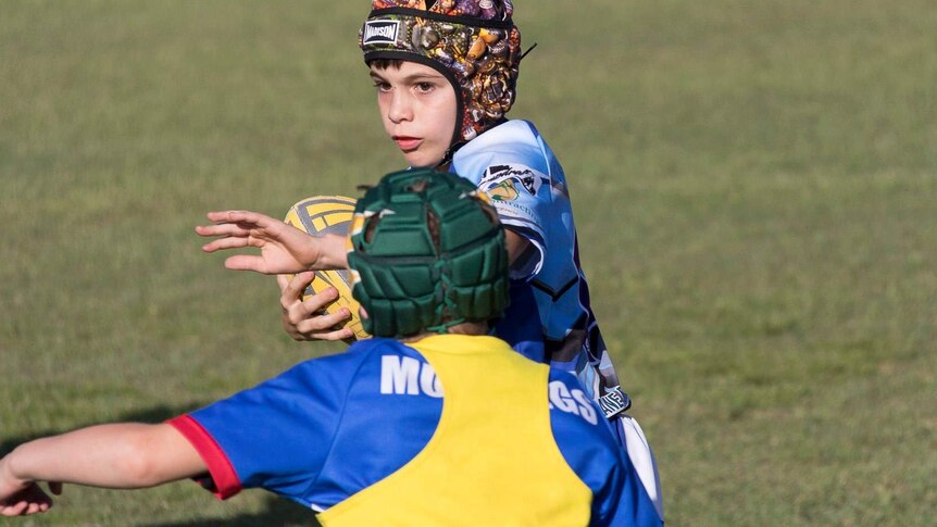 Little boy holding a football and dodges a tackle.