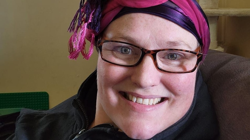 A close up of a widely smiling woman looks at the camera, wearing a pink headscarf.