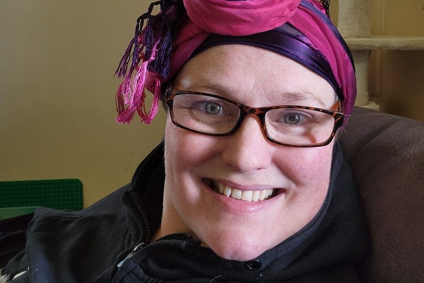 Anna Malcolm looks at the camera smiling wearing a pink headscarf 