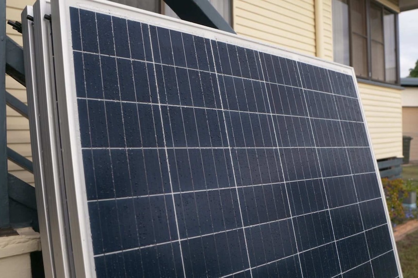 Solar panels leaning against the side of a weatherboard house waiting to be installed