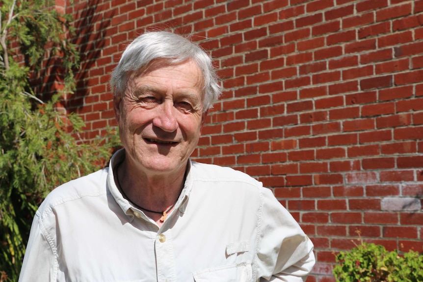 An older man squints at the camera outside what looks like a faculty building.