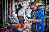 A man wearing a cloth face mask and blue jumper puts fruit into a bag while shopping.